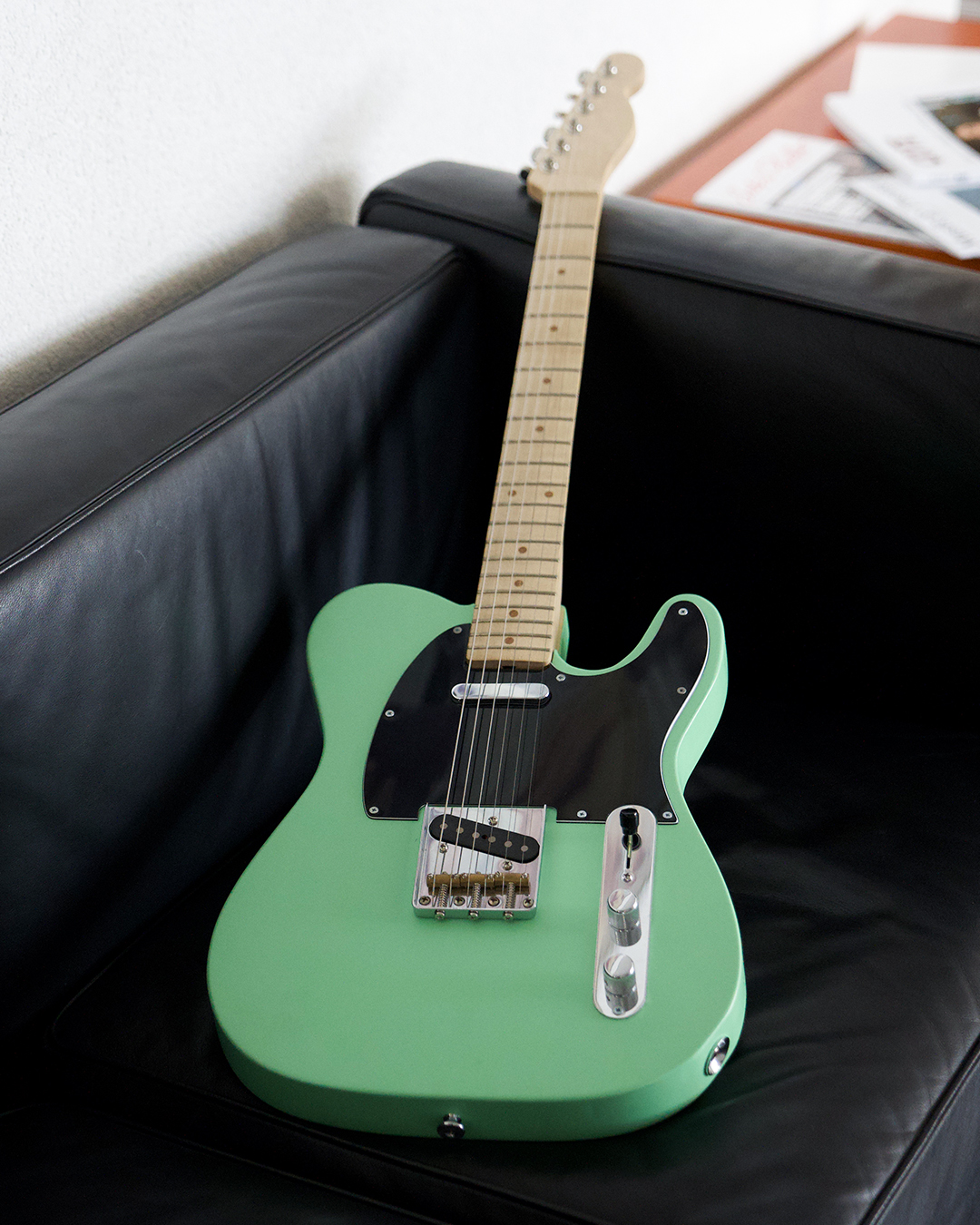 Eine mintgrüne E-Gitarre lehnt an einem schwarzen Ledersofa.