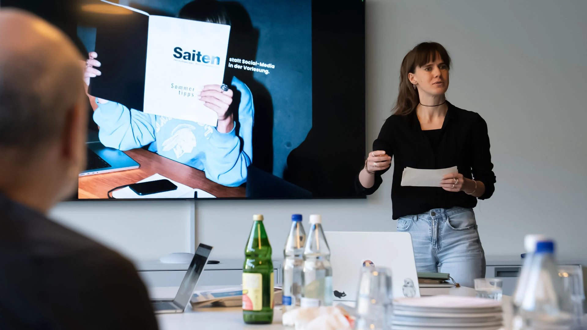 Daria Frick vom Kulturmagazin «Saiten» präsentiert in einem Sitzungszimmer vor einem Bildschirm mit einem «Saiten»-Heft, im Vordergrund ein Zuhörer.