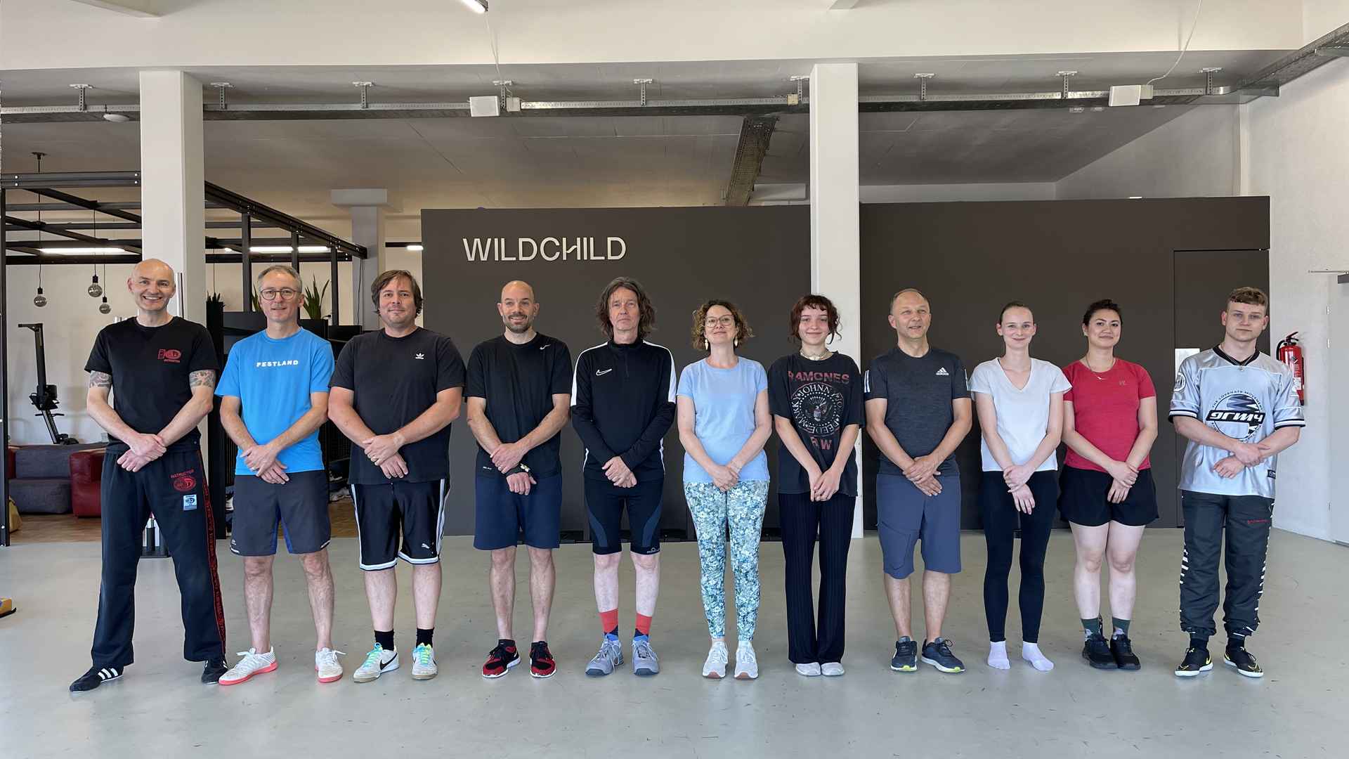 Zwölf Personen in Sportkleidung stehen in einer Reihe in einer Trainingshalle mit dem Schriftzug «Wildchild» an der Wand.