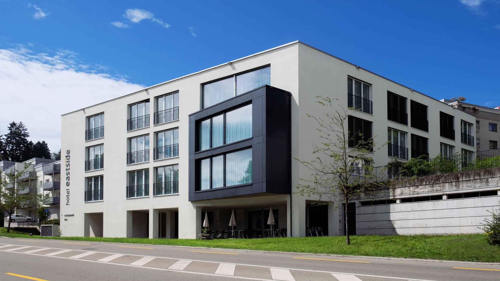 Moderner weisser Hotelbau mit dunkler Glasfassaden-Box und Schriftzug «hotel eastside» unter blauem Himmel, davor eine Strasse.
