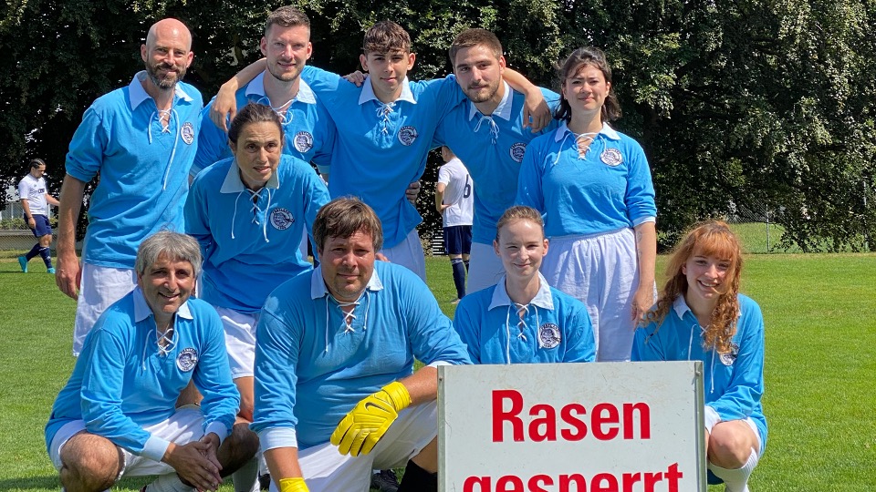 Festland-Fussballteam in hellblauen Retro-Trikots posiert für ein Gruppenfoto, vorne ein Schild mit der Aufschrift «Rasen gesperrt»