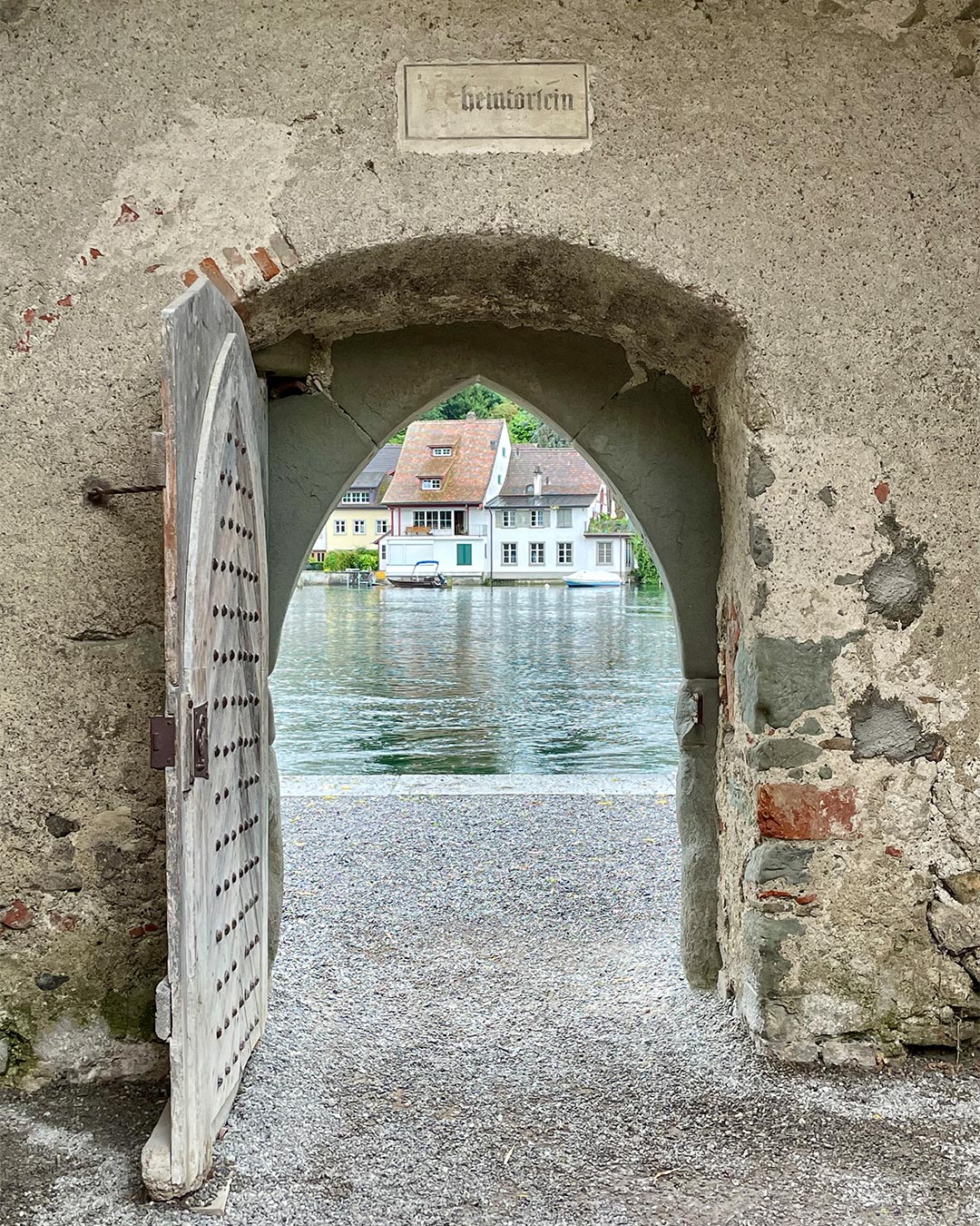 Blick durch ein offenes Stadttor mit der Aufschrift «Rheintörlein» auf den Rhein und die Häuser am gegenüberliegenden Ufer