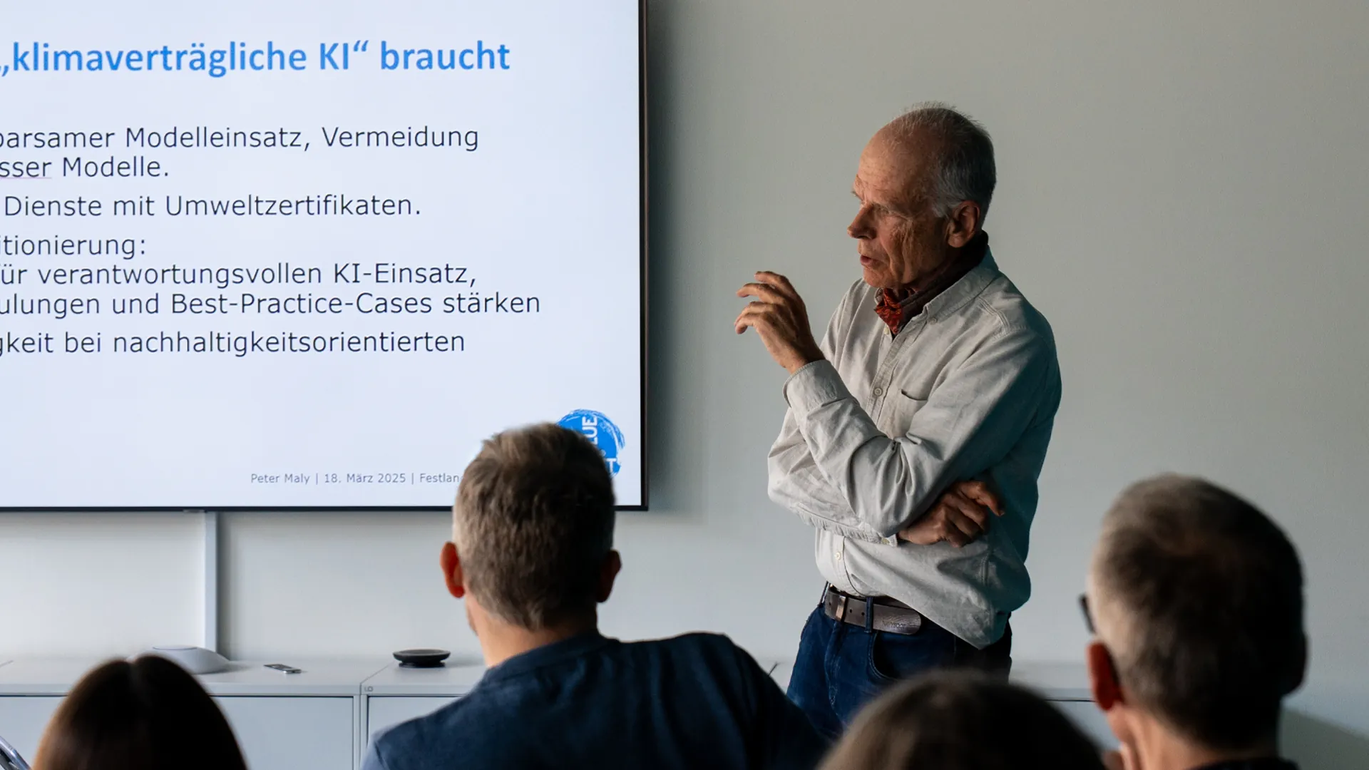 Referent Peter Maly spricht vor Publikum neben einer Präsentationsfolie zum Thema «klimaverträgliche KI».
