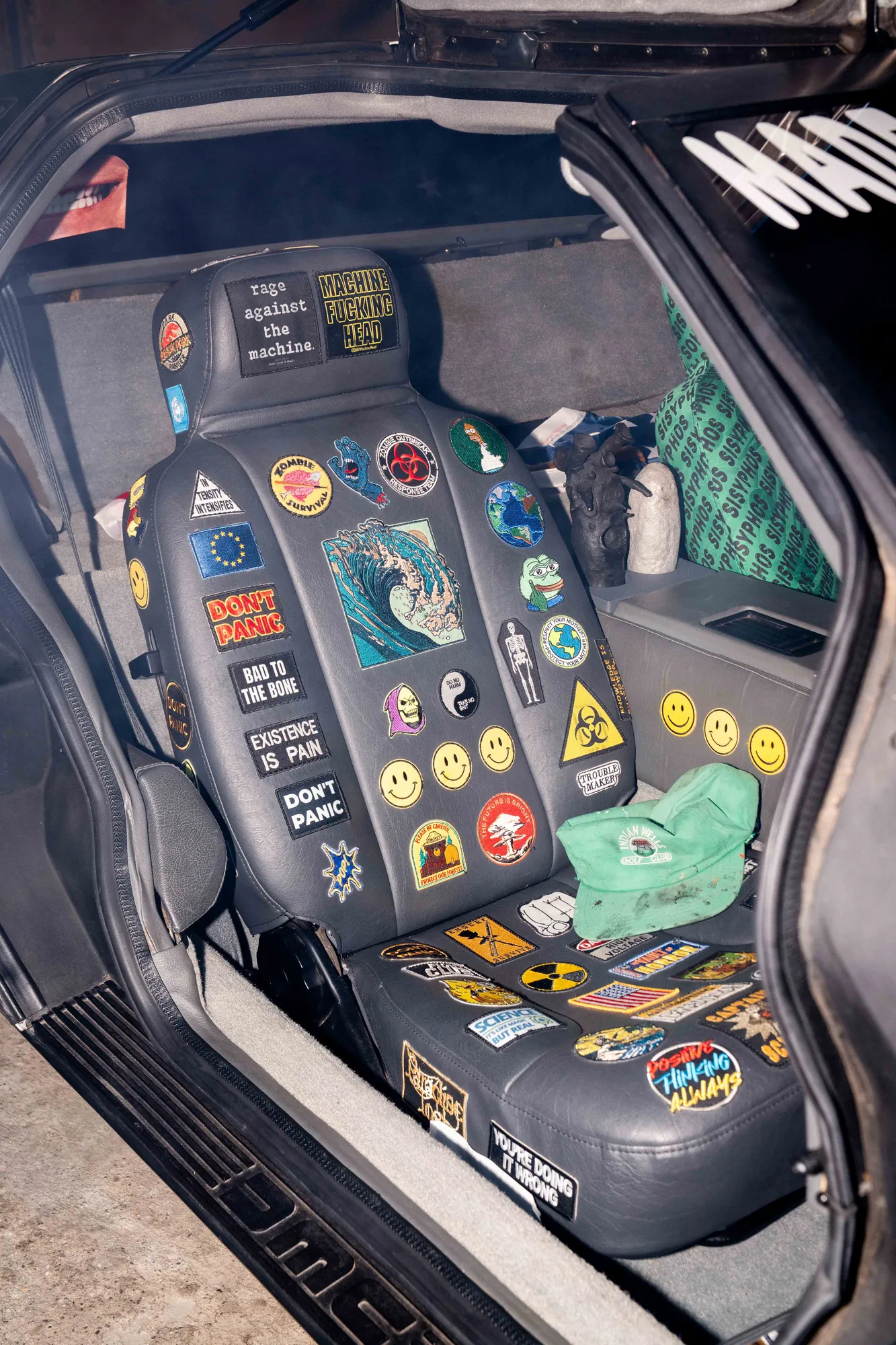 Autositz eines Sportwagens mit geöffneter Flügeltür, übersät mit Aufnähern und Stickern wie «Don't Panic», «Bad to the Bone» und gelben Smileys.