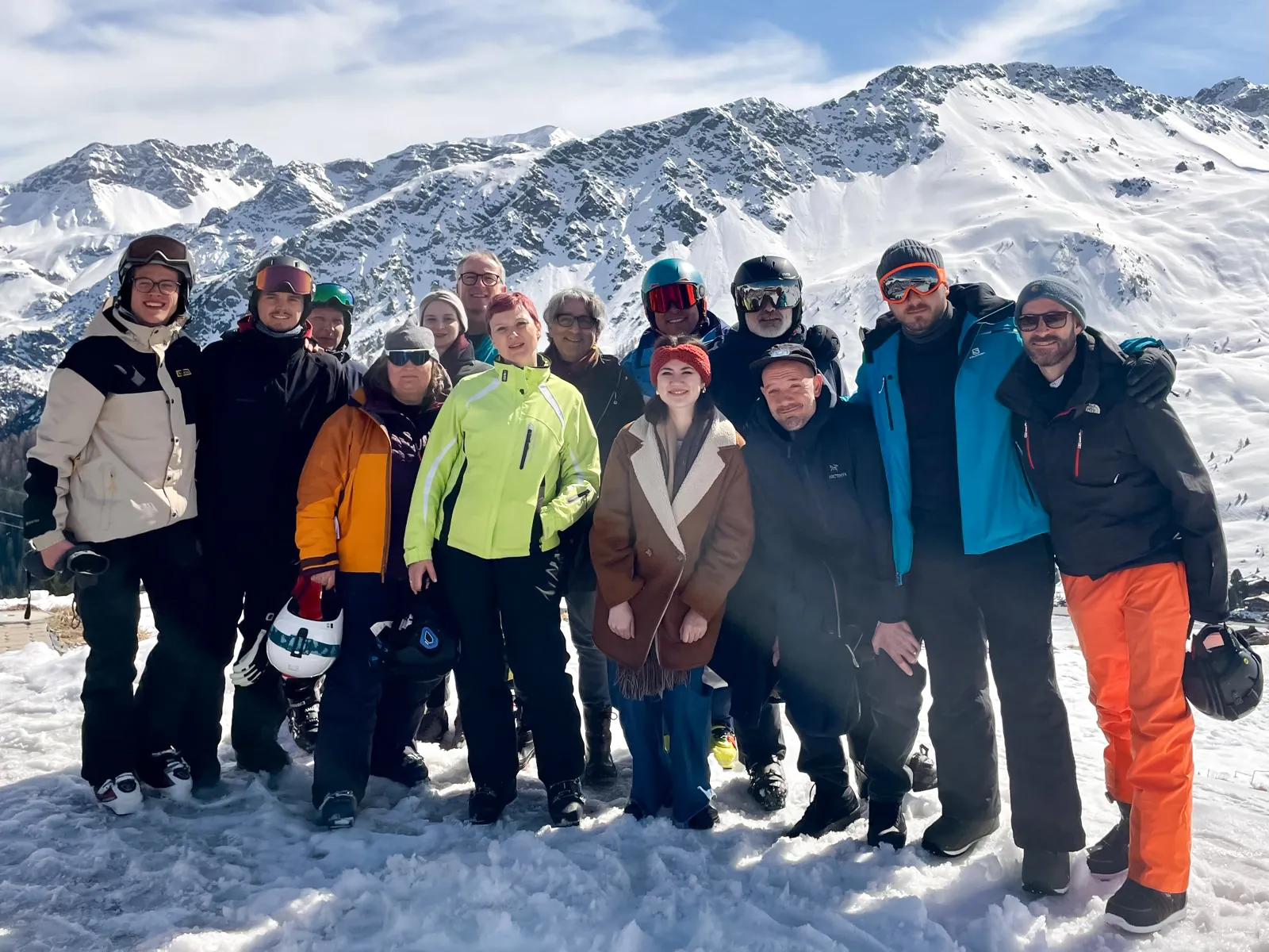 Gruppe in farbigen Skijacken und mit Helmen posiert im Schnee vor sonnigen, verschneiten Berggipfeln in Arosa.