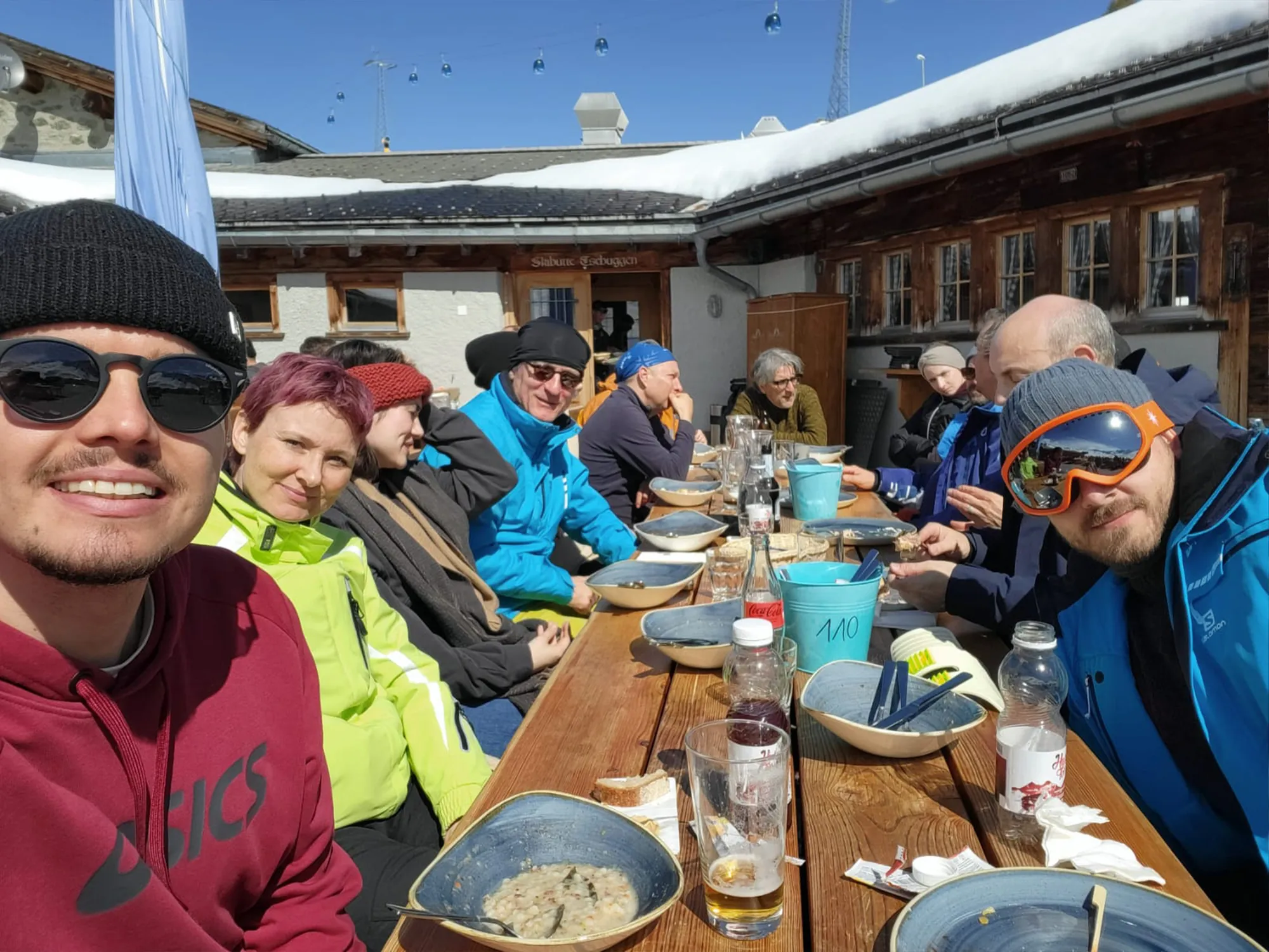 Das Festland-Team sitzt beim Zmittag an einem langen Holztisch vor einer Berghütte in der Wintersonne