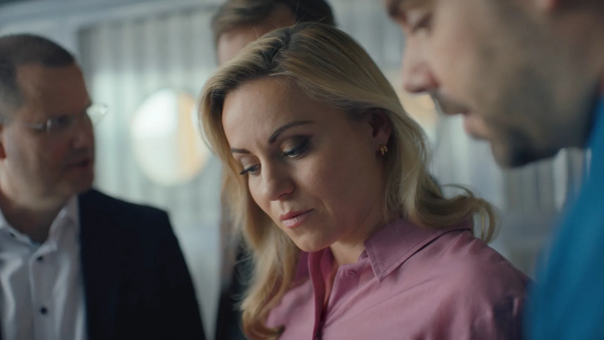 Filmstill der EY-Kampagne: Mitarbeiterin in rosa Bluse blickt mit Kollegen konzentriert nach unten – EY Professionals im Fokus