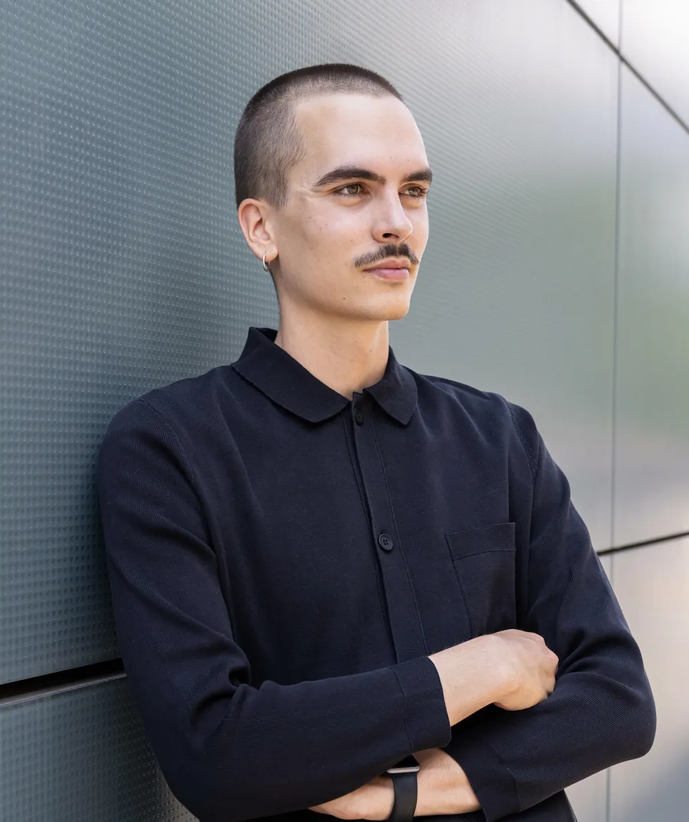 Porträt von Grafik- und Motion Designer Fabian Luginbühl, der mit verschränkten Armen an einer grauen Fassade lehnt