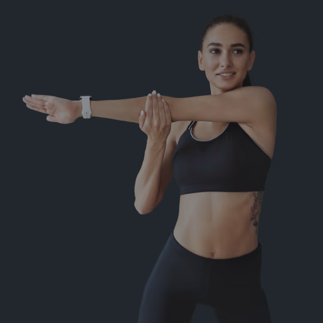 Young woman in athletic wear stretching her arm across her chest against a dark background.