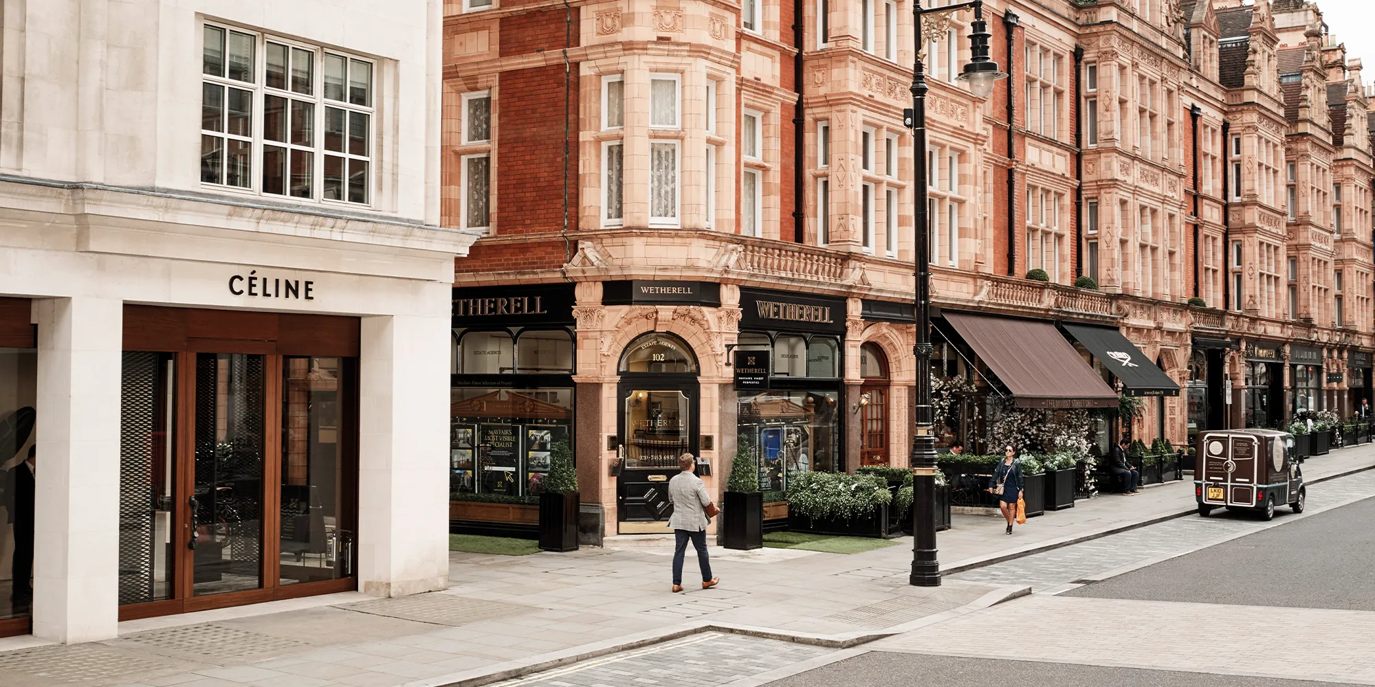 A scenic street view showcasing luxury storefronts, including Celine and Wetherell, with elegant red-brick buildings and pedestrians.