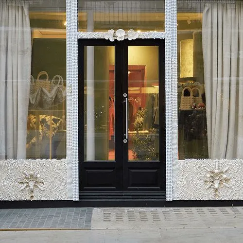 Elegant black storefront with pearl-adorned framing and decorative floral details, displaying bags and decor inside.