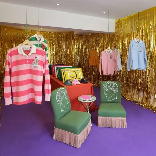 Boutique display featuring colorful striped shirts, green chairs with fringe, and a gold tinsel backdrop.