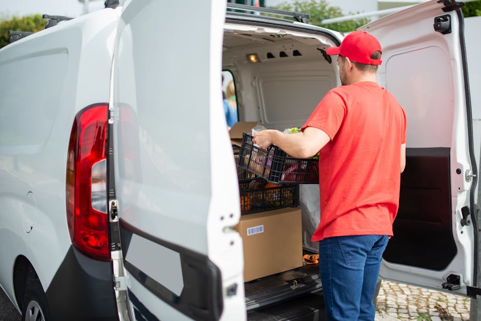 A courier in a red cap loads a delivery van with packages and a basket outdoors in Portugal.