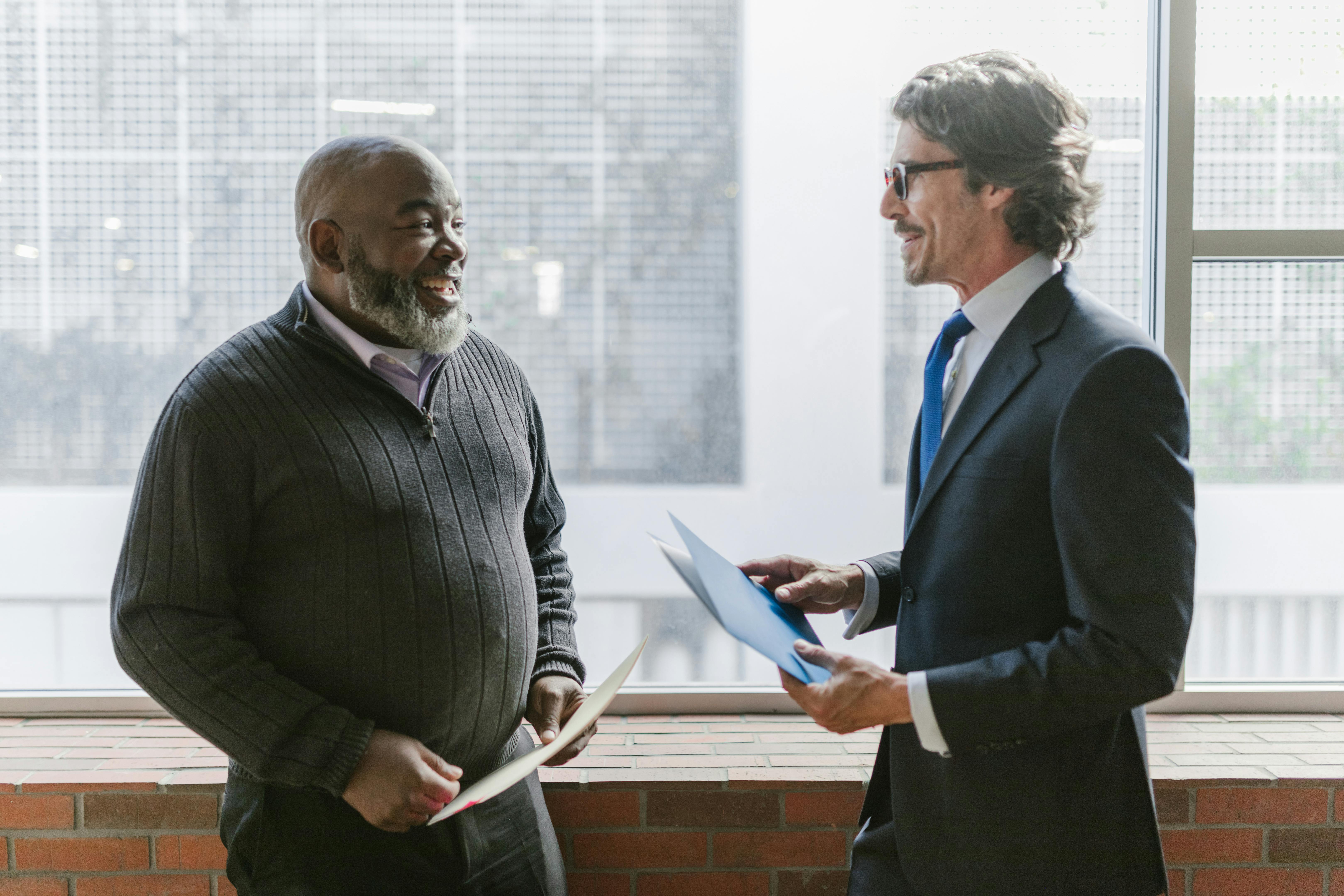 Two businessmen in a corporate setting engaging in a friendly conversation indoors.