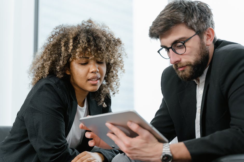 Two business professionals reviewing data on a tablet, fostering collaboration and teamwork in a modern office setting.