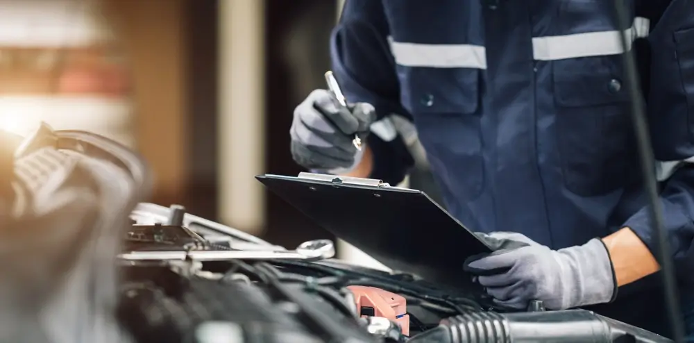 auto specialist holding clipboard and looking at car engine