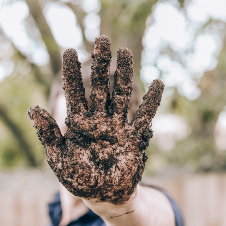 Close-up of a muddy hand reaching out for a high-five gesture in an outdoor environment.