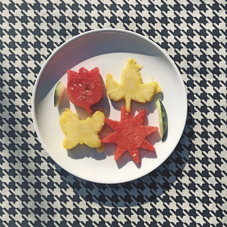 Watermelon and pineapple artfully cut and arranged on a white plate and set on a black and white patterned tablecloth.