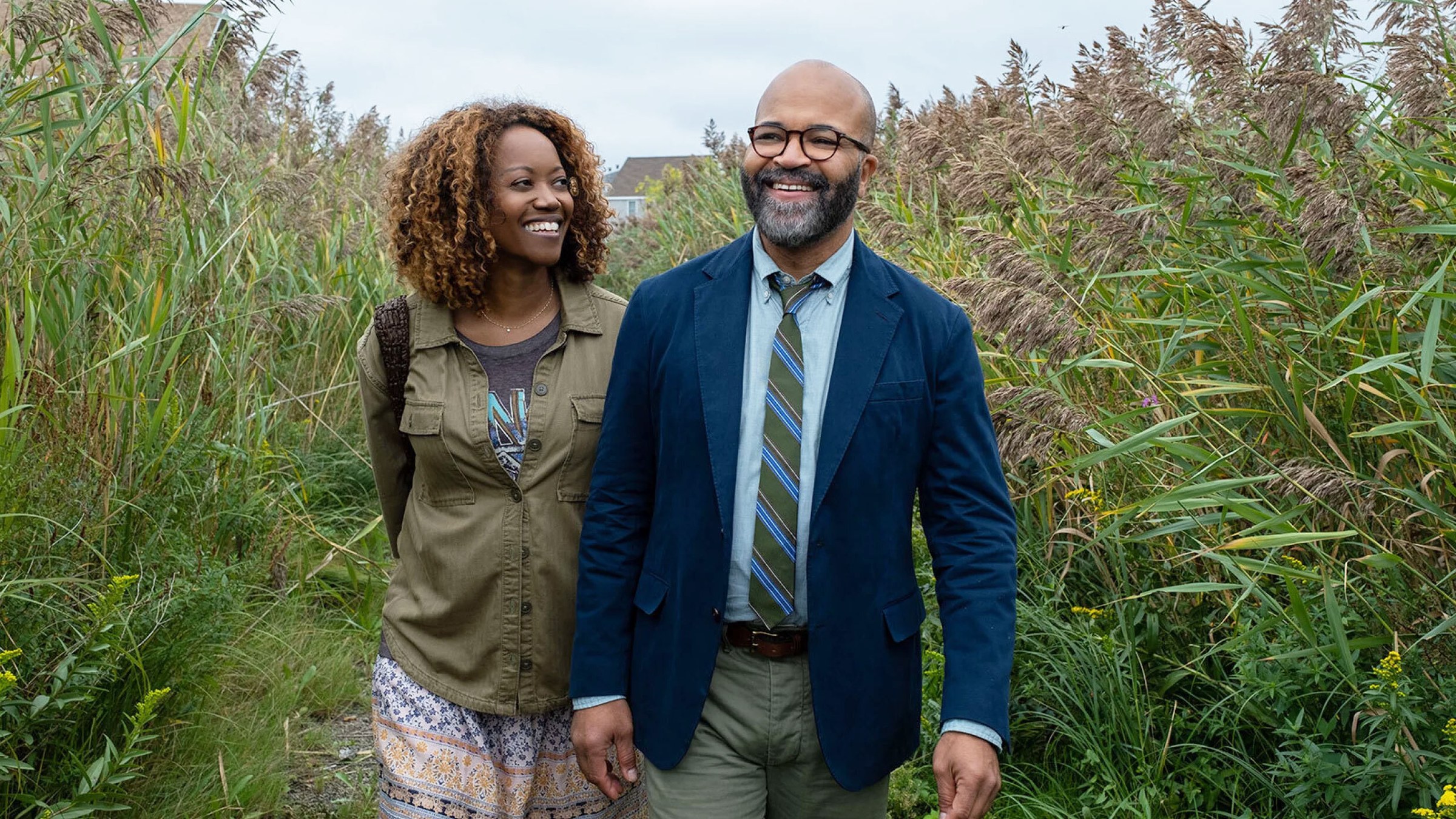 Jeffrey Wright and Erika Alexander walk hand in hand through tall grass in a scene from American Fiction.