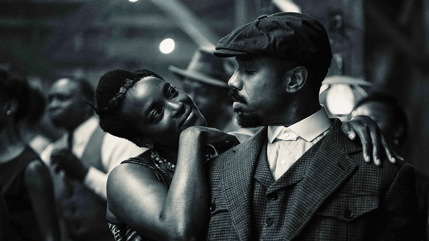 Wunmi Mosaku rests her head on Michael B. Jordan's shoulder in a crowded juke joint, in a black-and-white photo from Sinners.