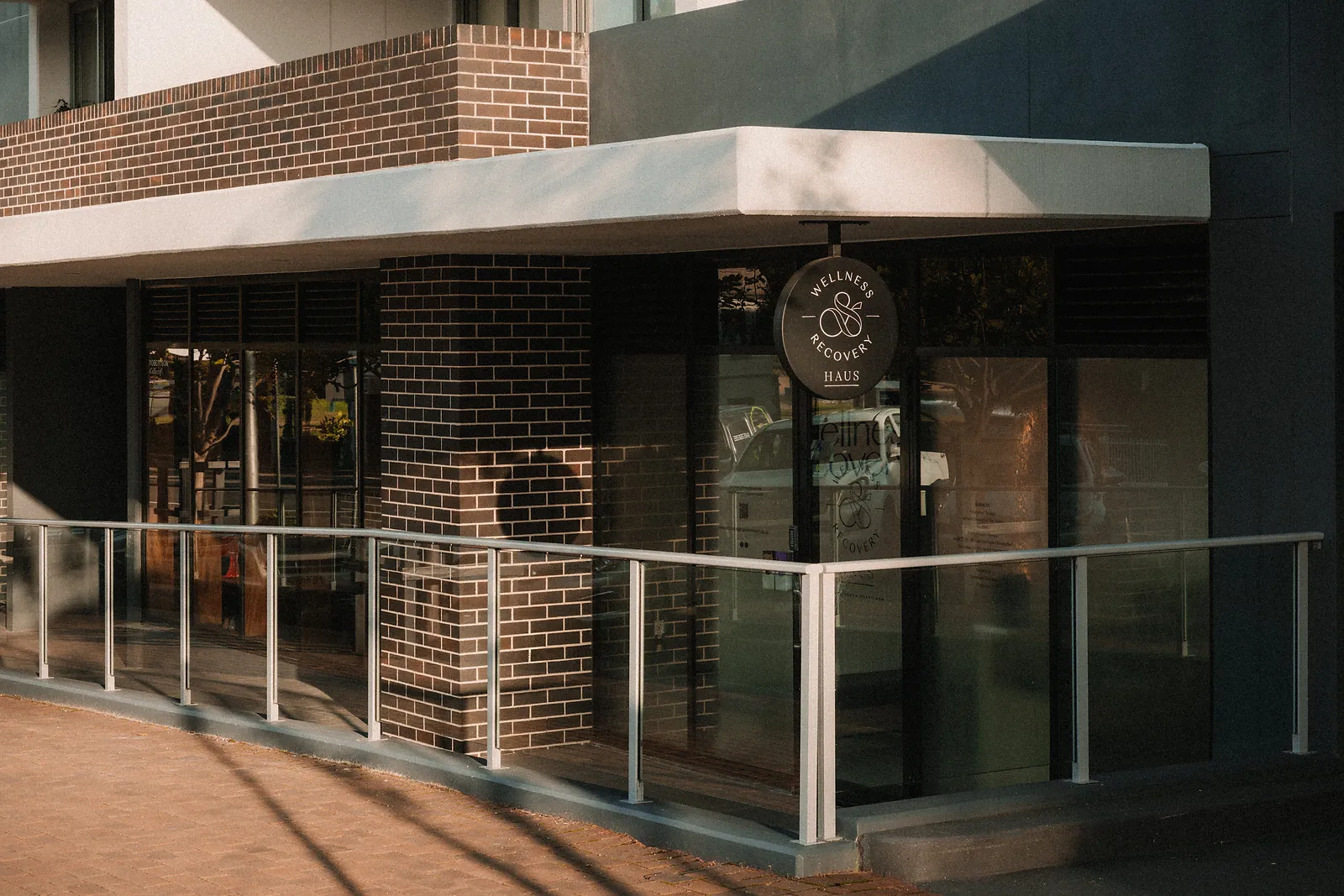 Entrance of Wellness Recovery Haus with glass door and brick walls, lit by soft sunlight.
