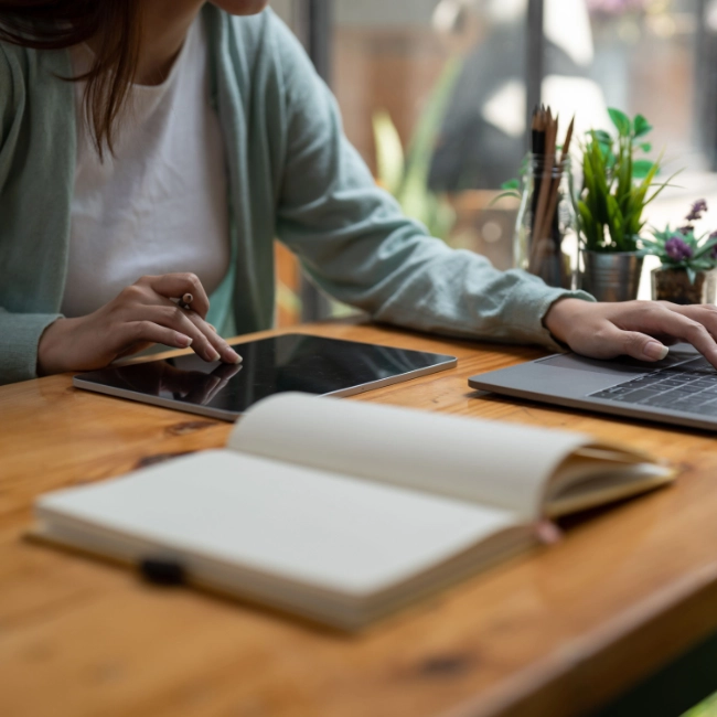 Personne suivant une formation en ligne sur tablette et ordinateur portable, carnet de notes ouvert.