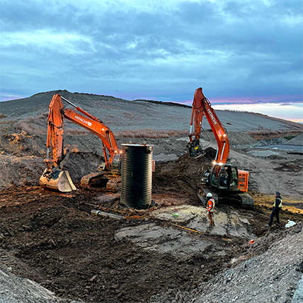 Completed landfill cell with graded clay-lined slopes, access road, and drainage infrastructure under winter conditions, viewed across an open prairie landscape.