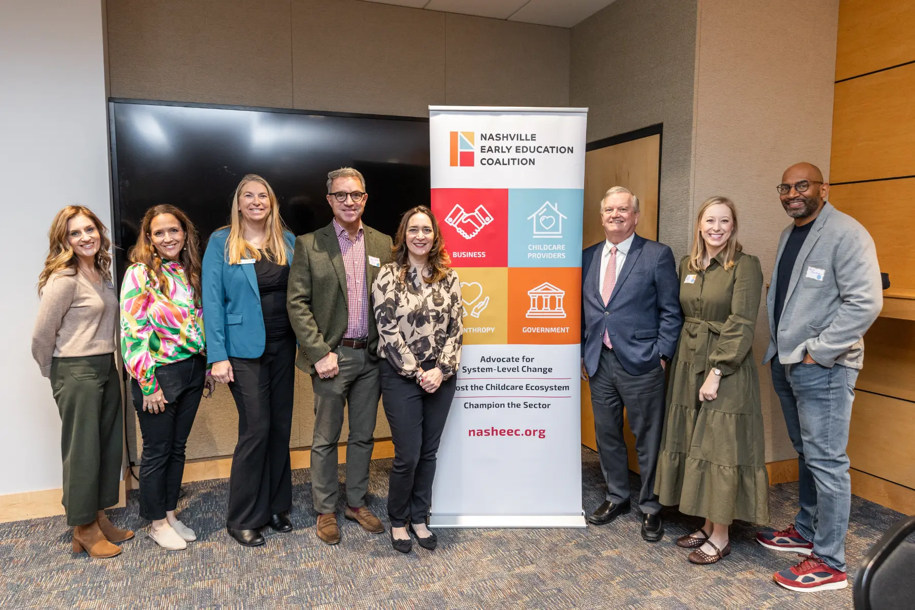 Six adults standing in a row smiling beside a Nashville Early Education Coalition banner in an indoor conference room.