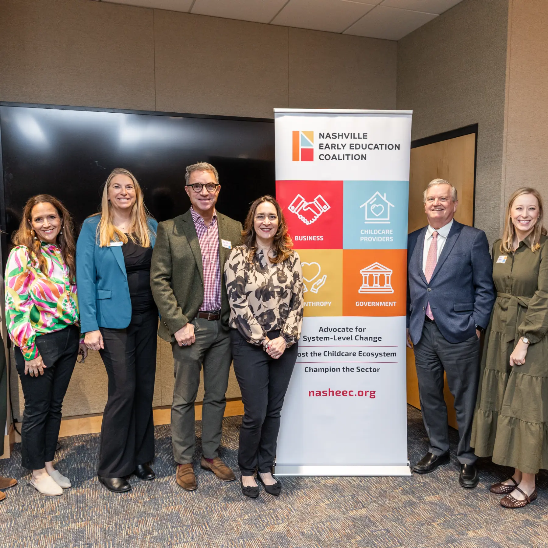Six adults standing in a row smiling beside a Nashville Early Education Coalition banner in an indoor conference room.