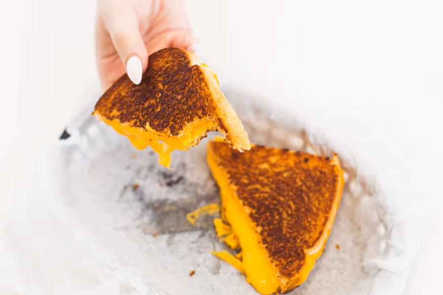 close up shot of a hand holding a melting grilled cheese sandwich 