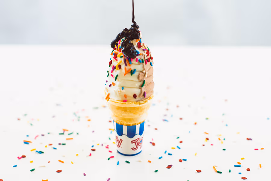 close up shot of a vanilla chocolate ice cream come being topped with chocolate syrup 