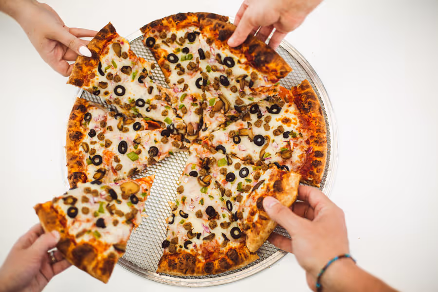 close up of various hands reaching in for a meat pizza 