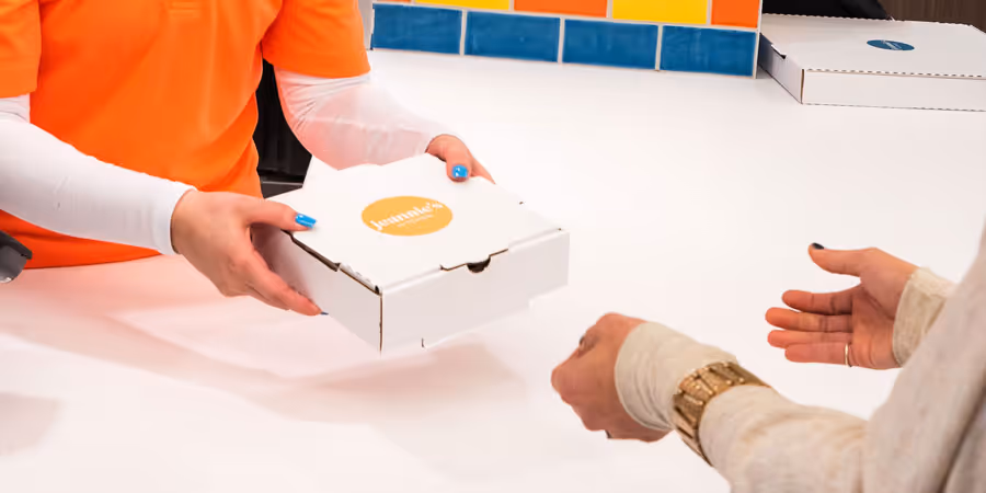 close up shot of jeannie's employee handing a jeannies branded pizza box to a customer