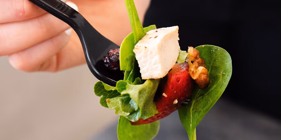close up of a hand holding a fork with salad