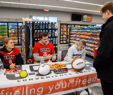 Young male talking with the members of the U-Stop team inside a U-Stop shop signing posters