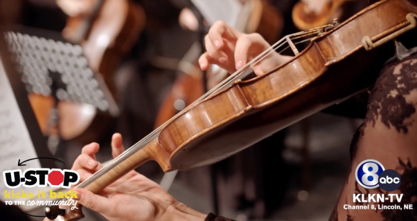 Close-up of hands playing a violin in an orchestra setting.