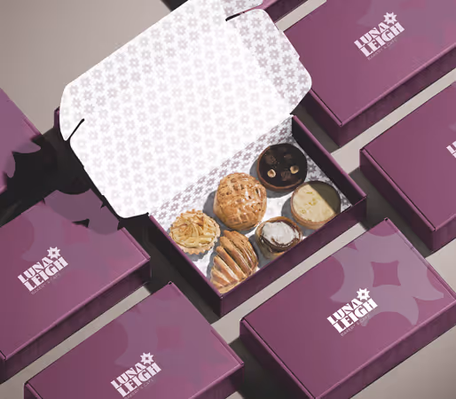 Open purple Luna Leigh box showing an assortment of six pastries surrounded by closed Luna Leigh boxes.
