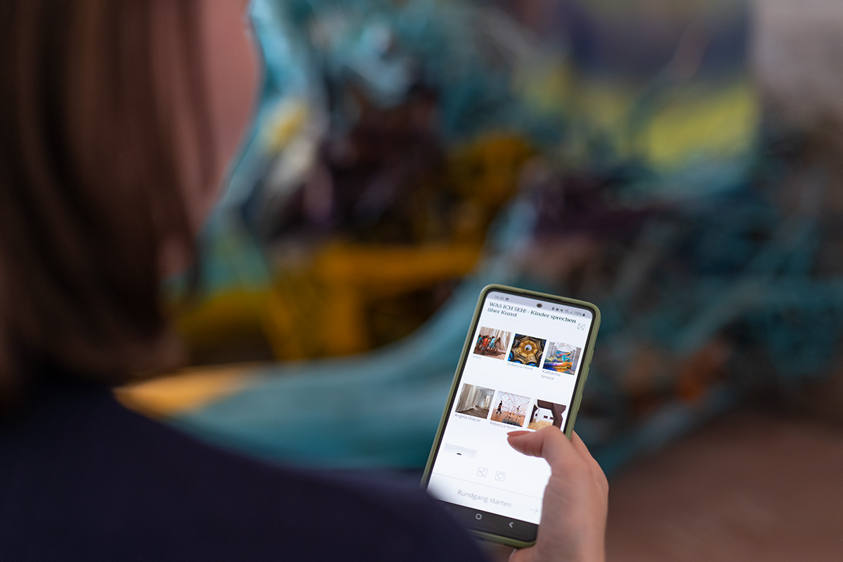 Eine Frau steht im Museum Wiesbaden vor einem Kunstwerk und betrachtet die Audioguides auf ihrem Handy