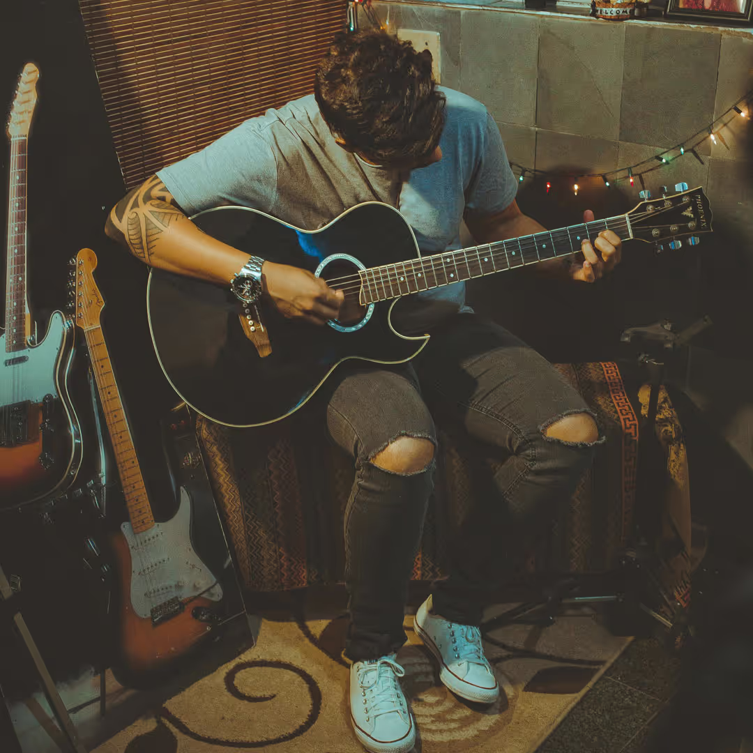 Man playing guitar in a room by himself as a form of guitar therapy.