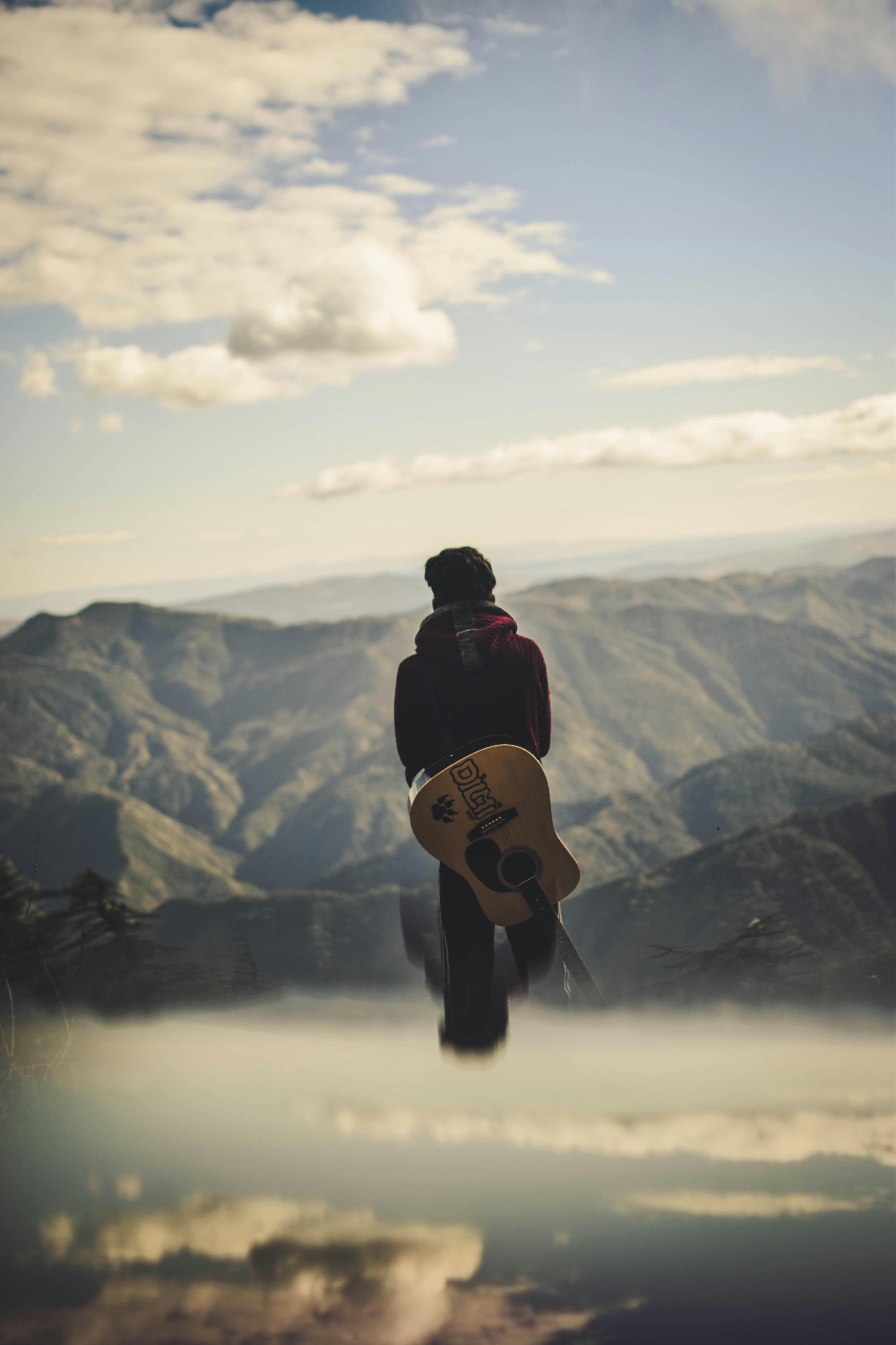 Man with guitar on back staring into the abyss of mountains
