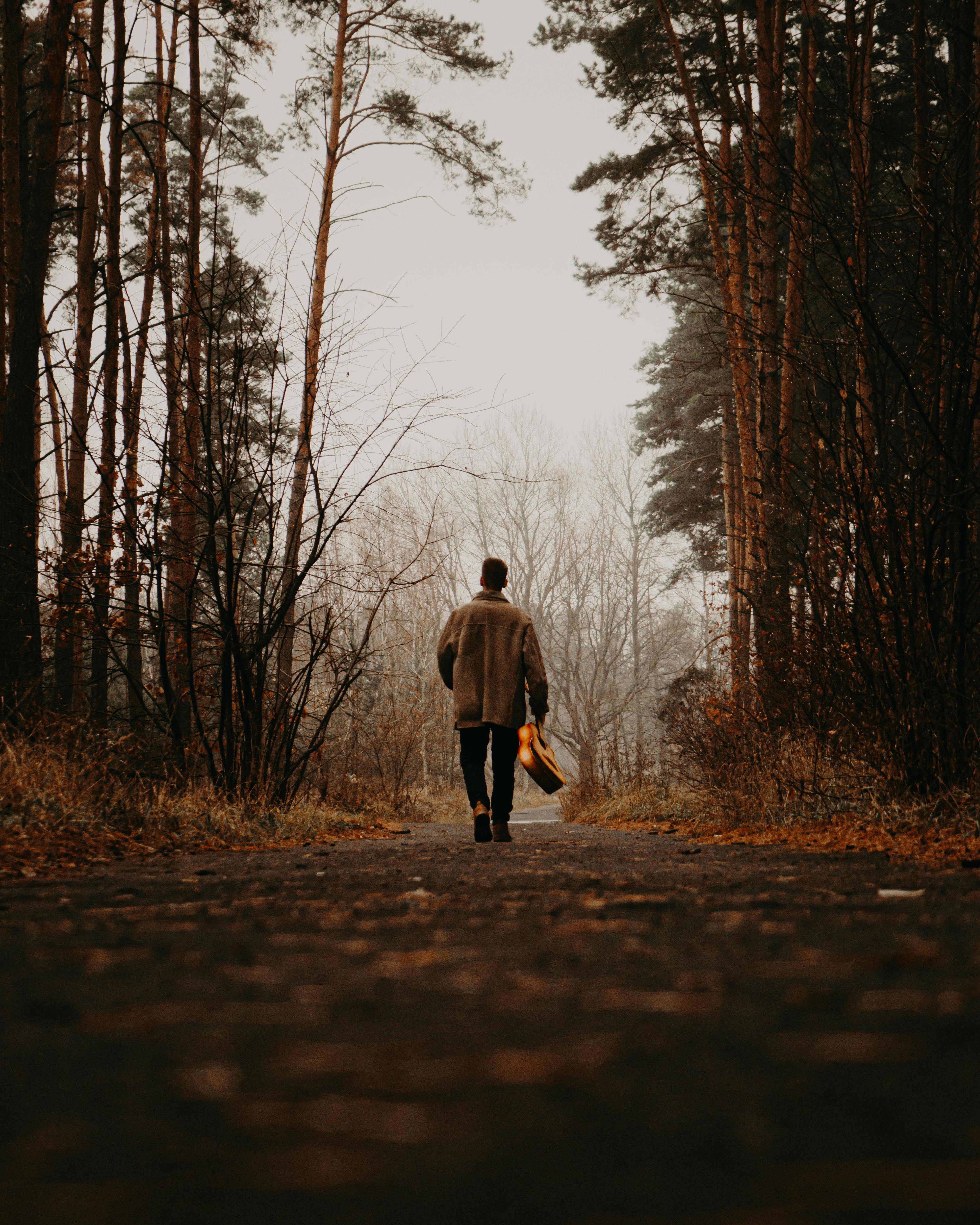 Man with guitar on back walking through the woods