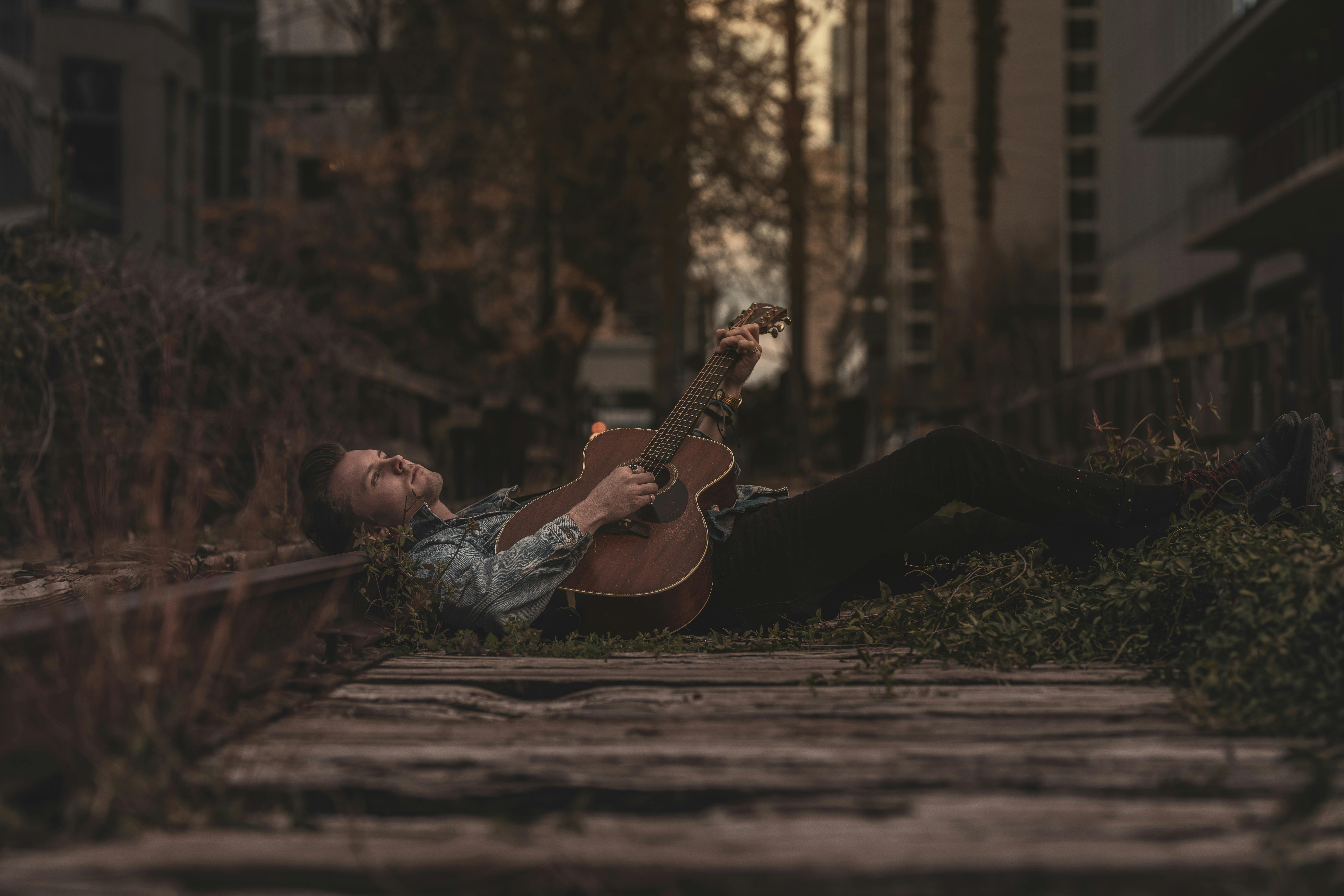 Man playin guitar laying down in a scenic environment