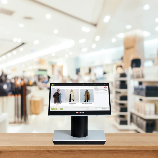 Pantalla de un sistema de punto de venta mostrando productos de ropa en una tienda moderna con estanterías y clientes desenfocados al fondo.