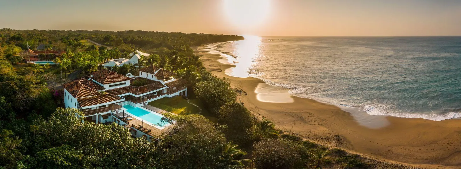 Beachfront villa with a pool above a long sandy beach at sunset