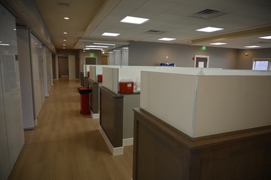 Office corridor with wooden flooring and a row of cubicles with white partition panels and wooden lower panels.