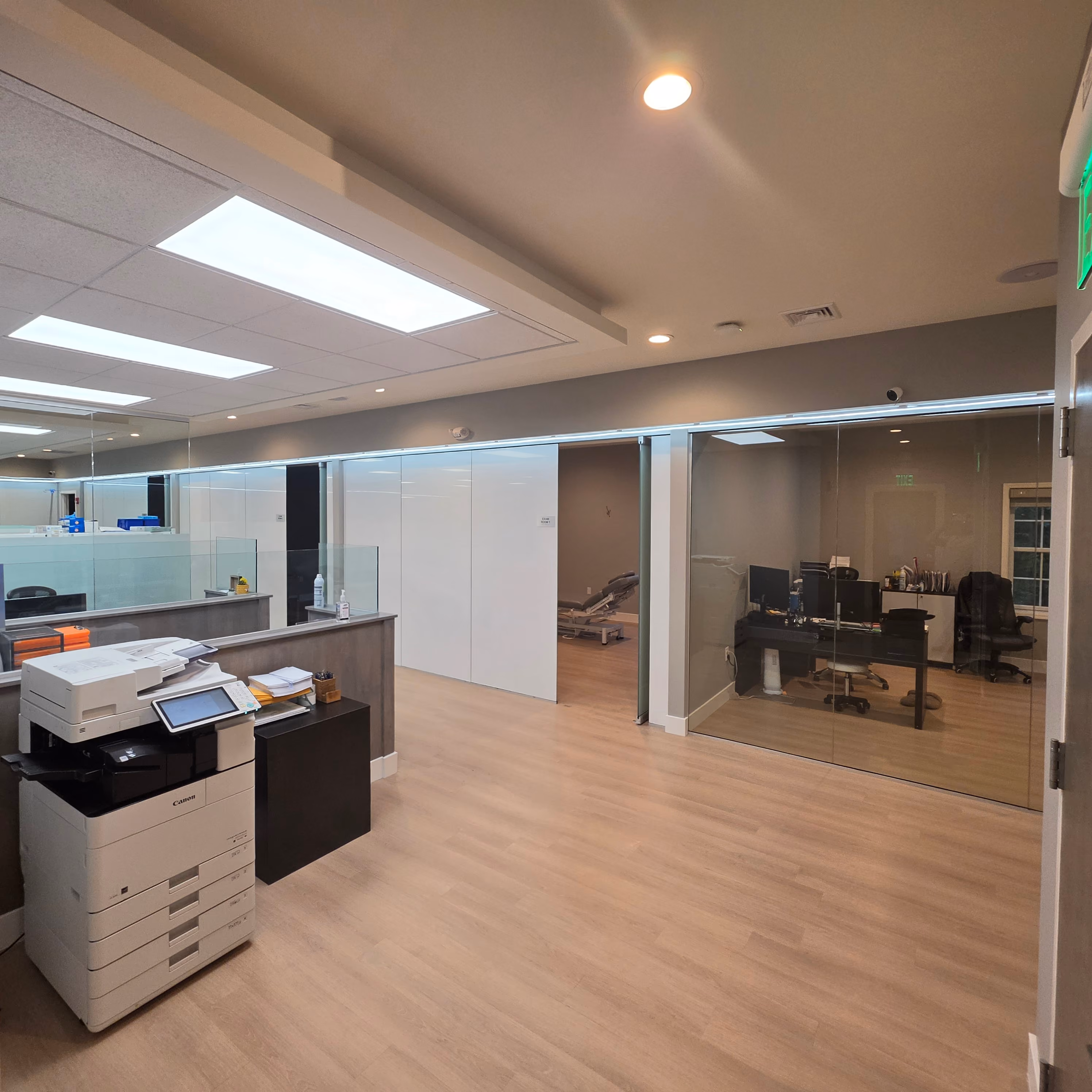 Empty modern office room with glass walls, wooden floor, desk, and ergonomic chair facing a window.