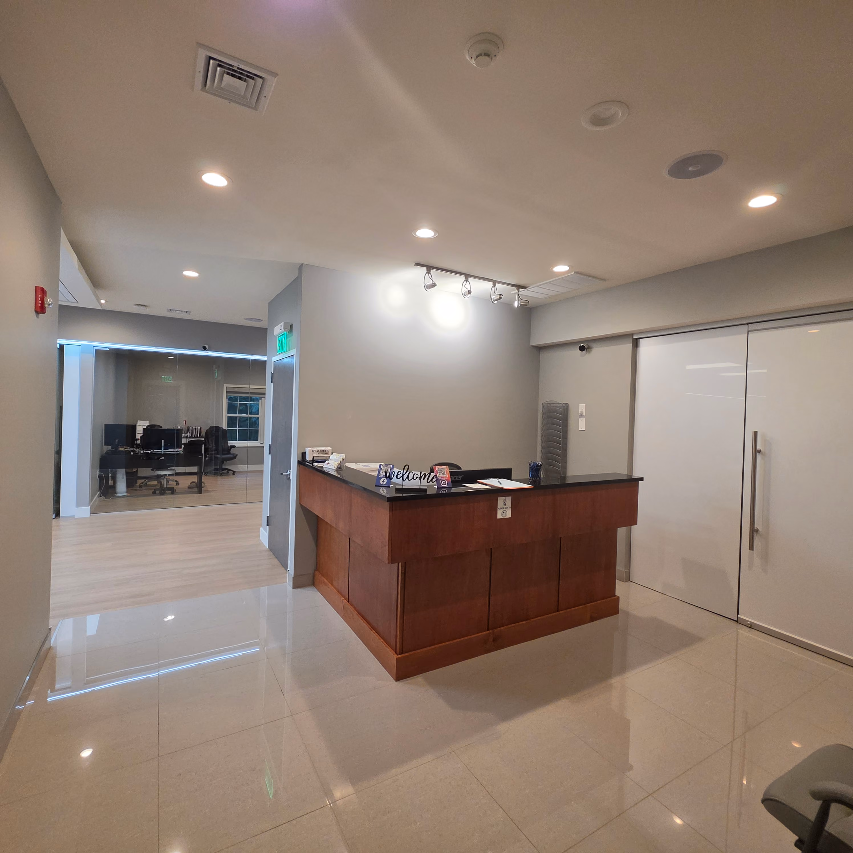 Reception desk with wooden base and black countertop, featuring a computer monitor, hand sanitizer, and a decorative bowl.