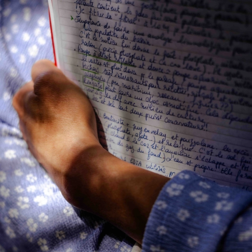  Main d'une participante prenant des notes manuscrites dans un cahier lors d'une formation en transformation alimentaire, illustrant l'apprentissage pratique et théorique.