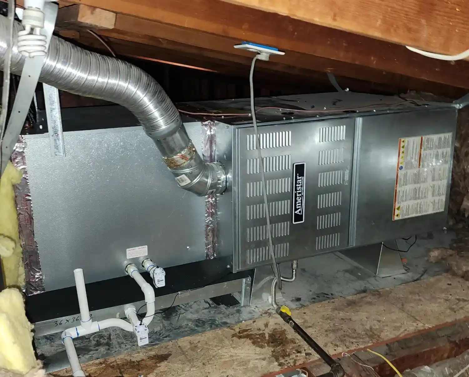 A metal Ameristar HVAC unit in an attic with exposed wooden beams and ductwork.