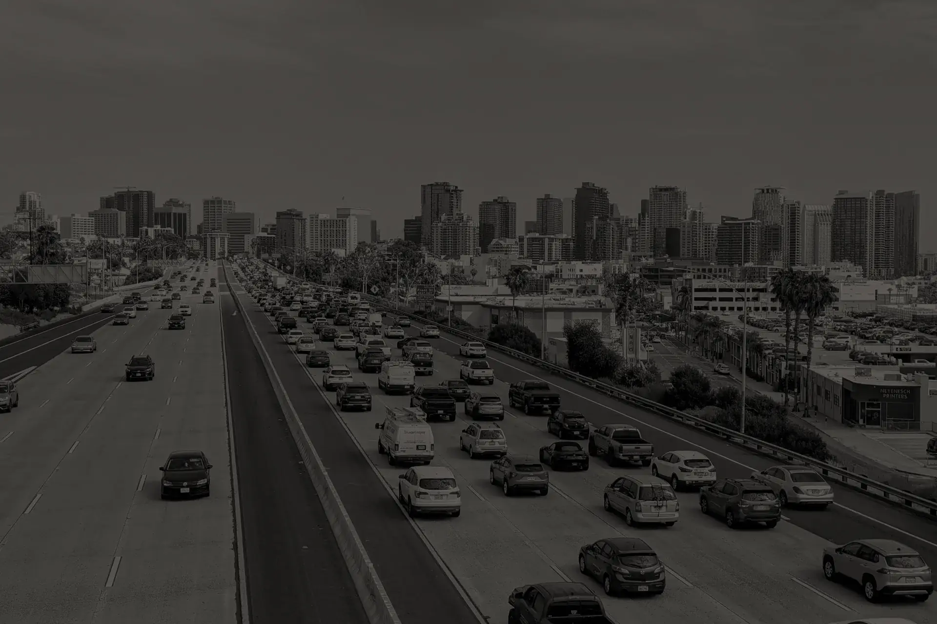 Busy multi-lane highway with city skyline in the background under a cloudy sky.